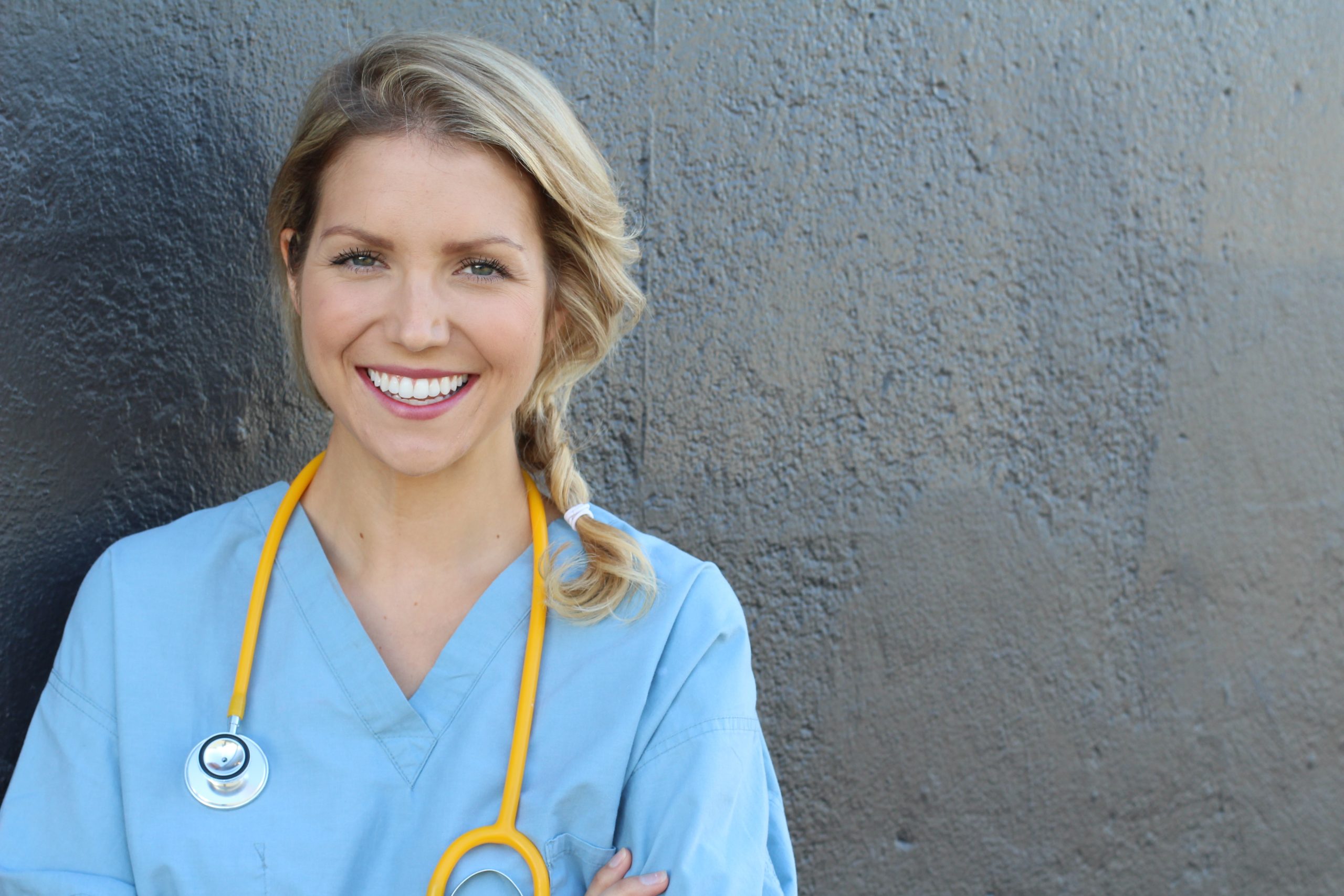 Infirmière souriante adossée a un mur